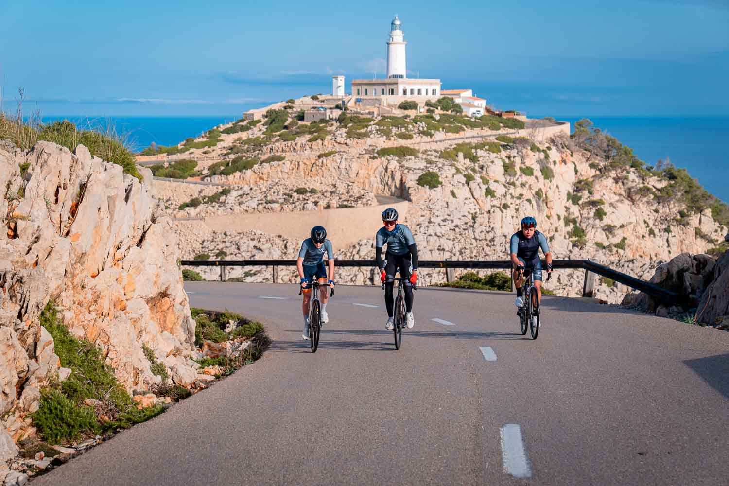 Three Velocamp cyclists with lighthouse behind