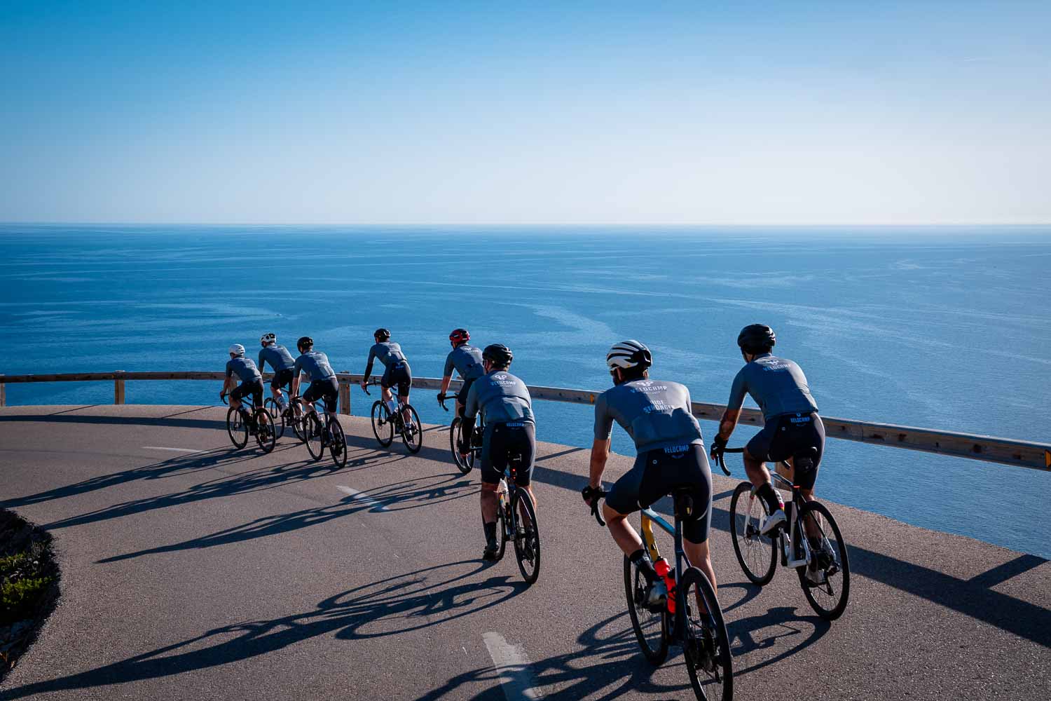 Velocamp peloton descending with ocean behind
