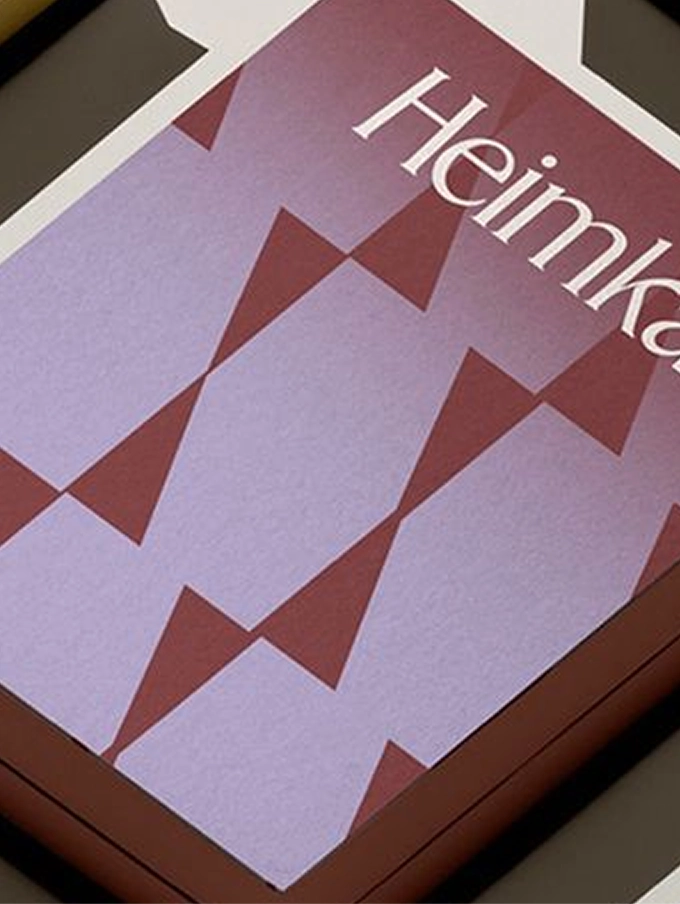 Poster with geometric pattern of overlapping brown and lavender triangles and partial white text reading 'Heimka'.