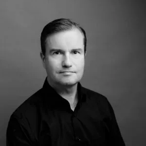 Black and white portrait of a man in a dark shirt against a plain background.