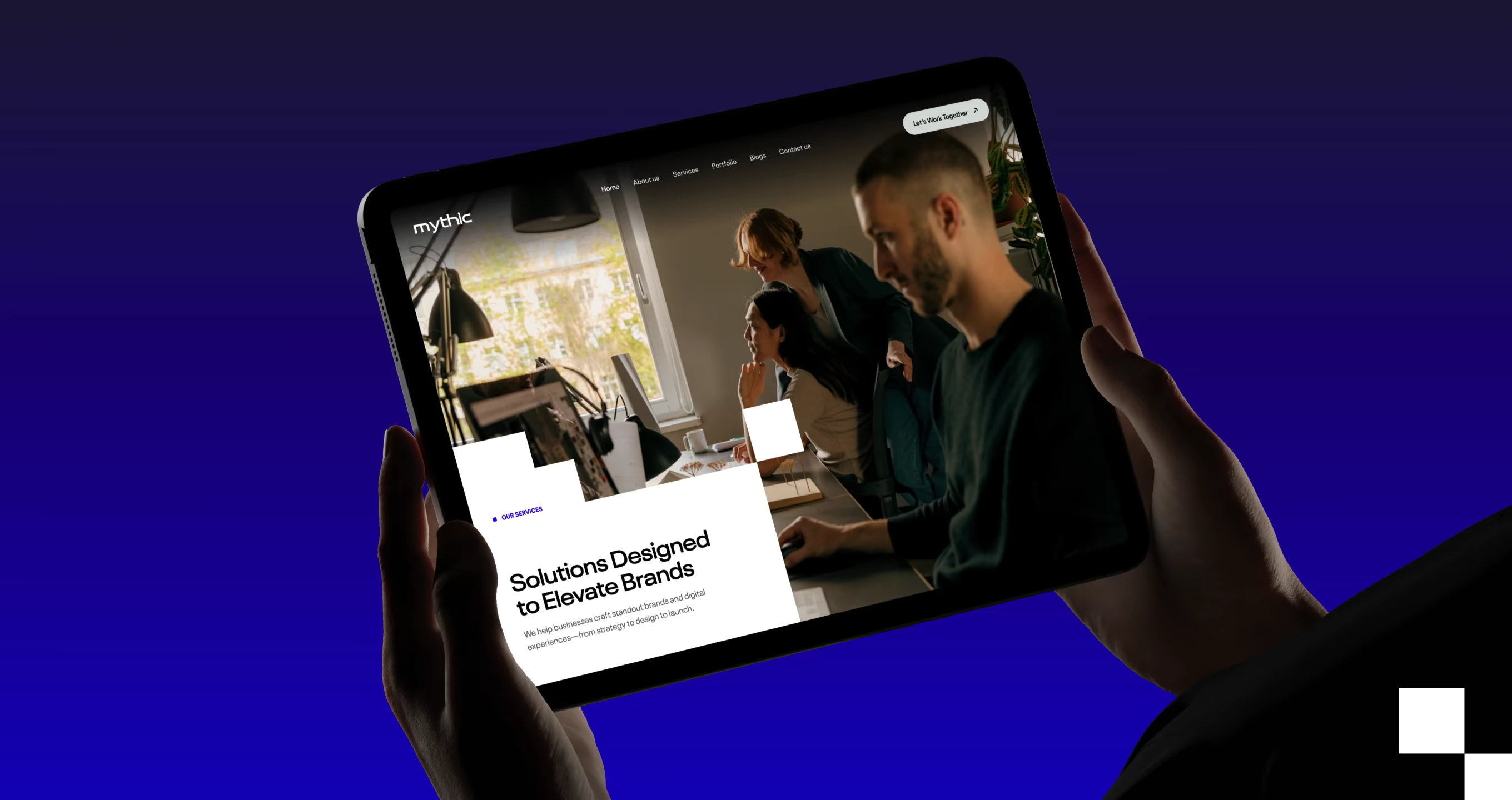Person holding a tablet displaying a website with a group of people working in an office and the text 'Solutions Designed to Elevate Brands.'