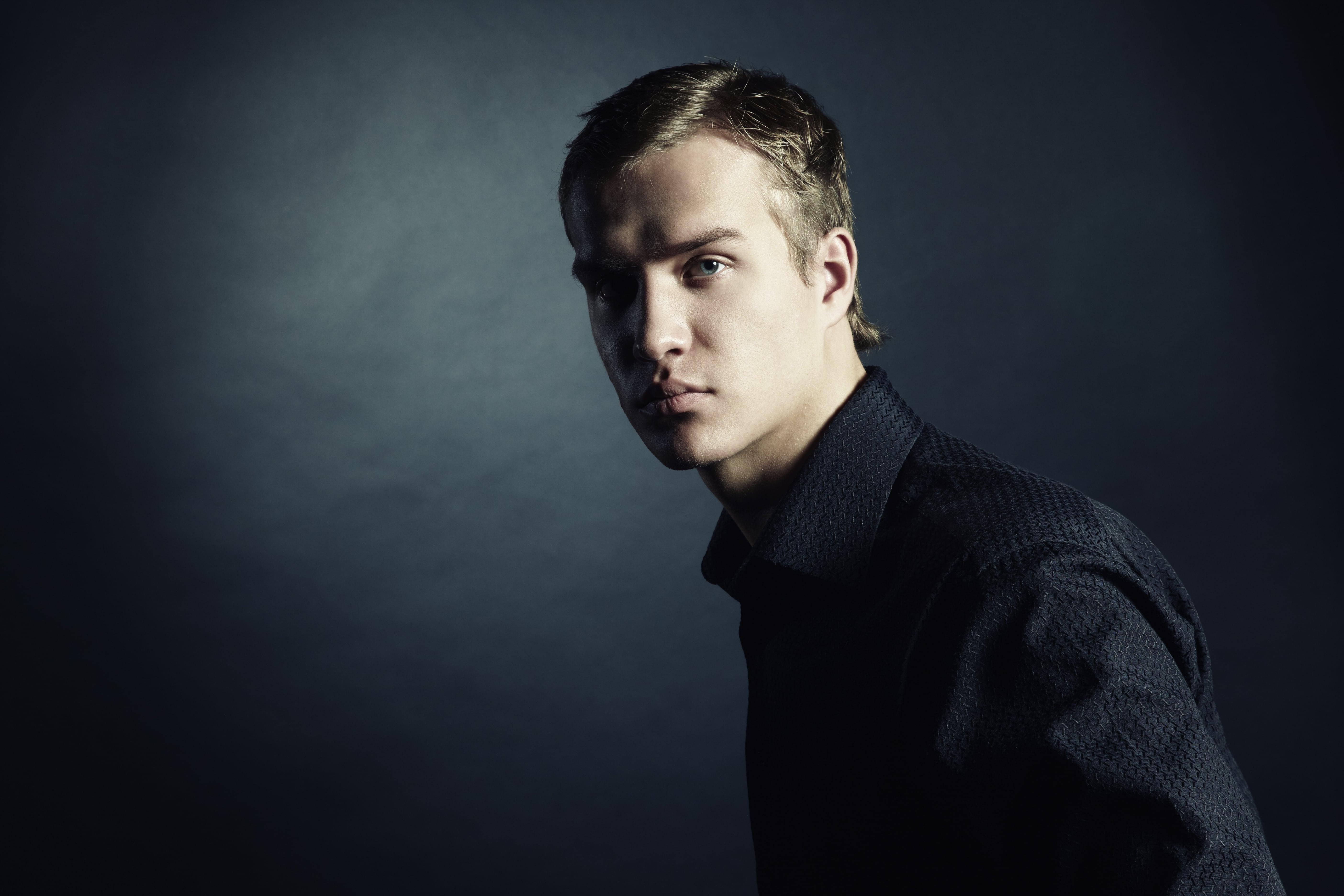 Young person in dark sweater looking to the side against moody background