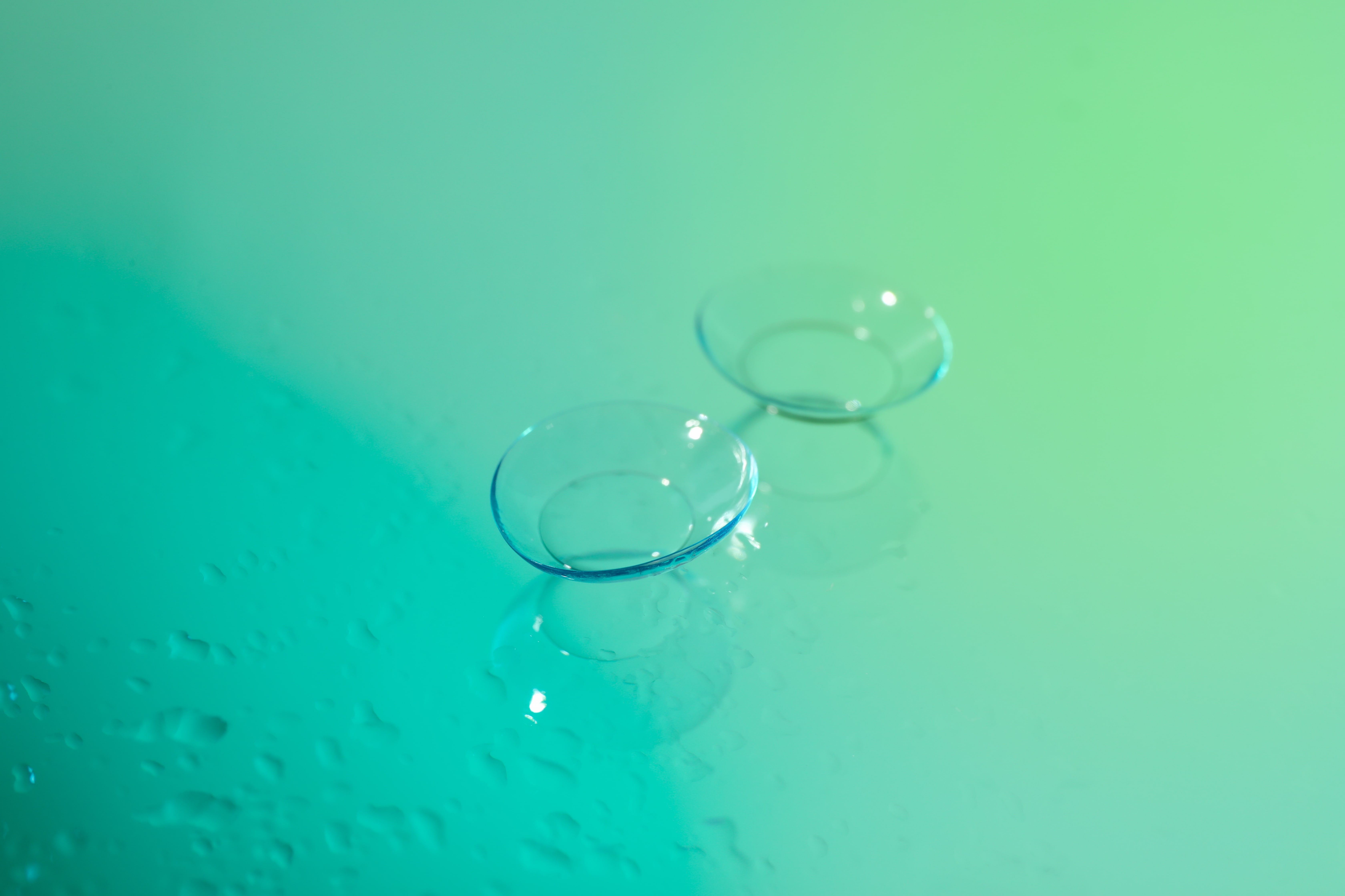 Contact lenses floating on a turquoise and green gradient background