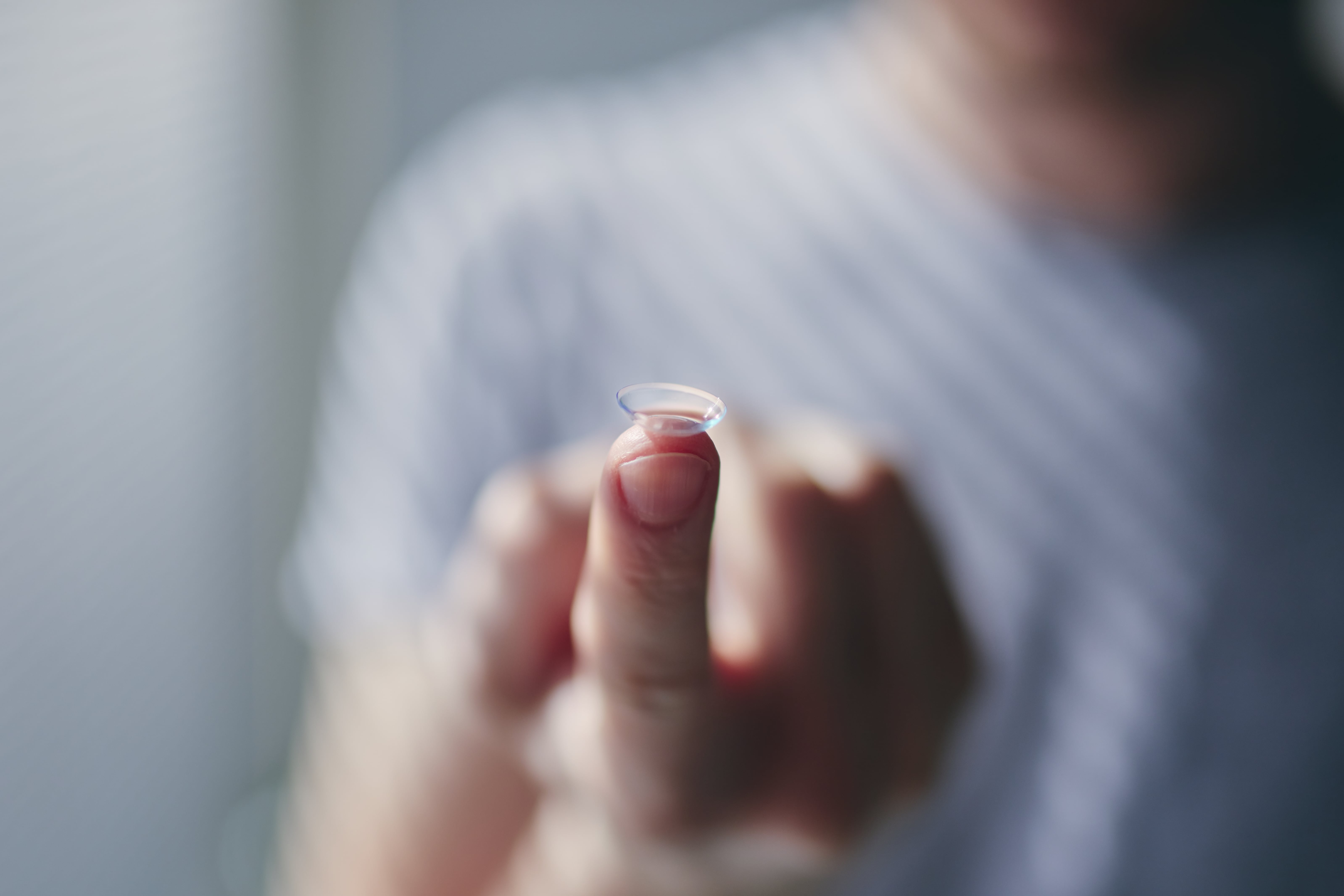 Transparent contact lens balanced on fingertip against blurred background