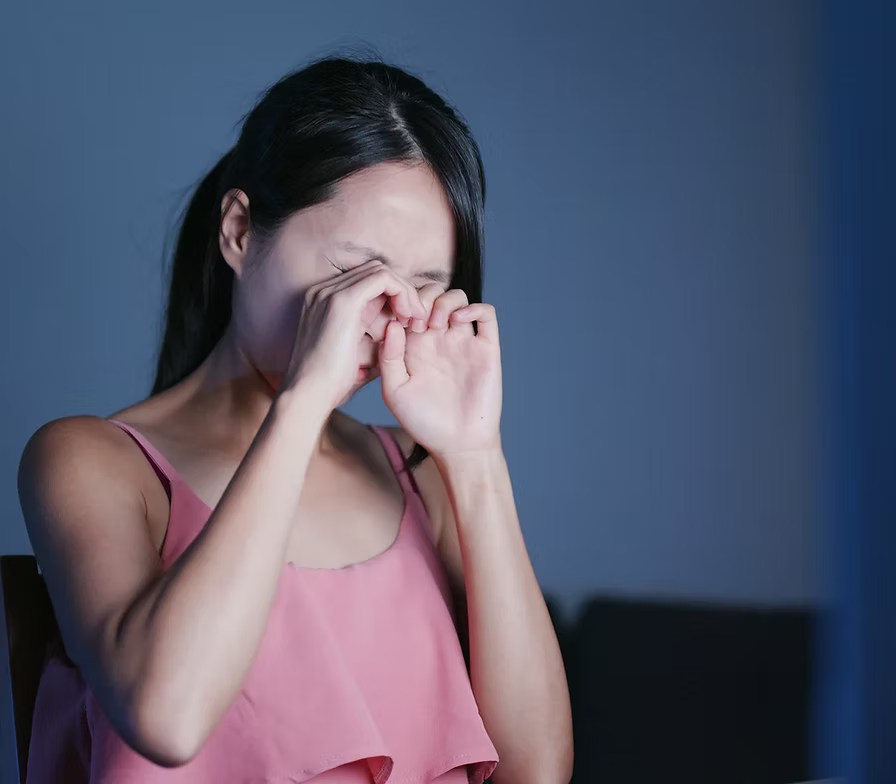 Person in pink top rubbing eyes, looking distressed or tired