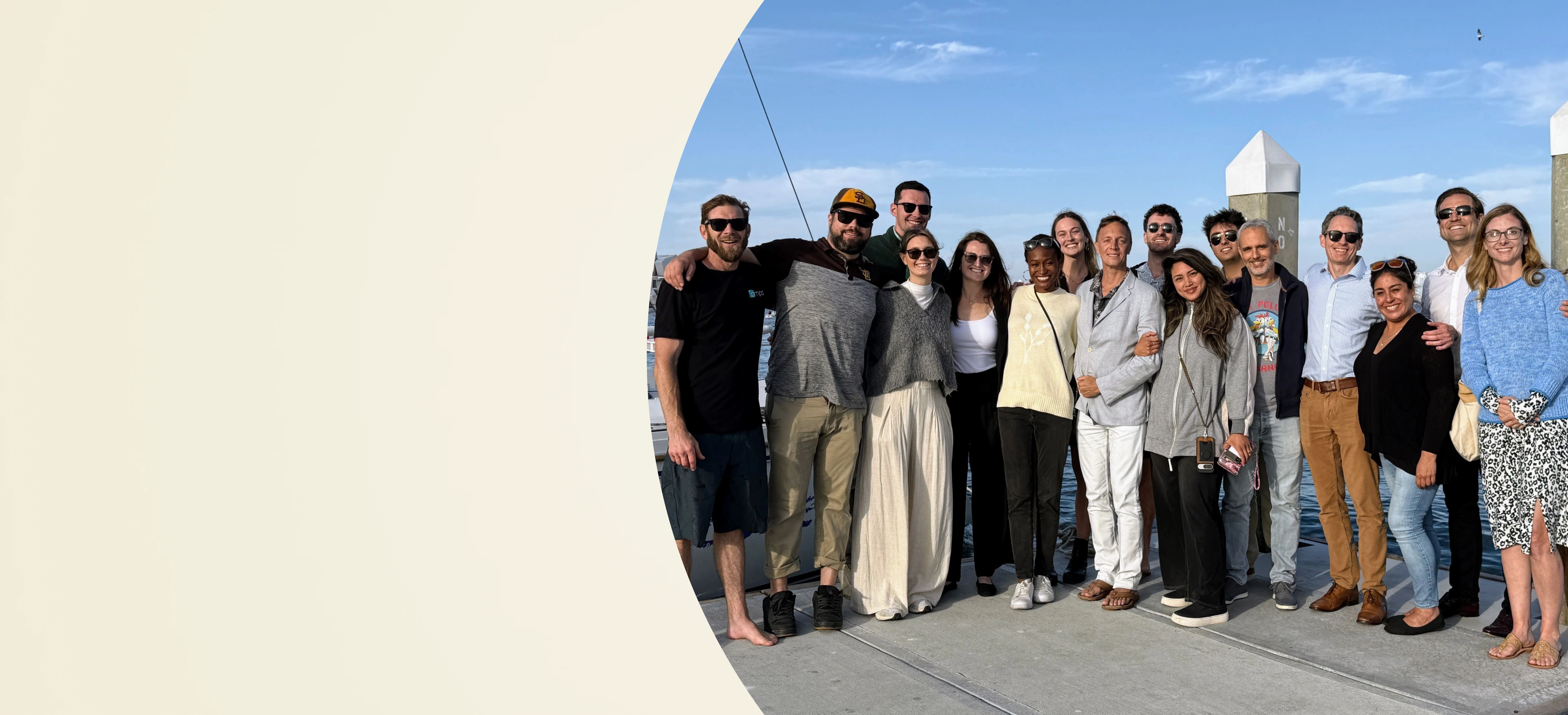 Group of diverse people standing closely, smiling outdoors on a sunny day near water and docks.