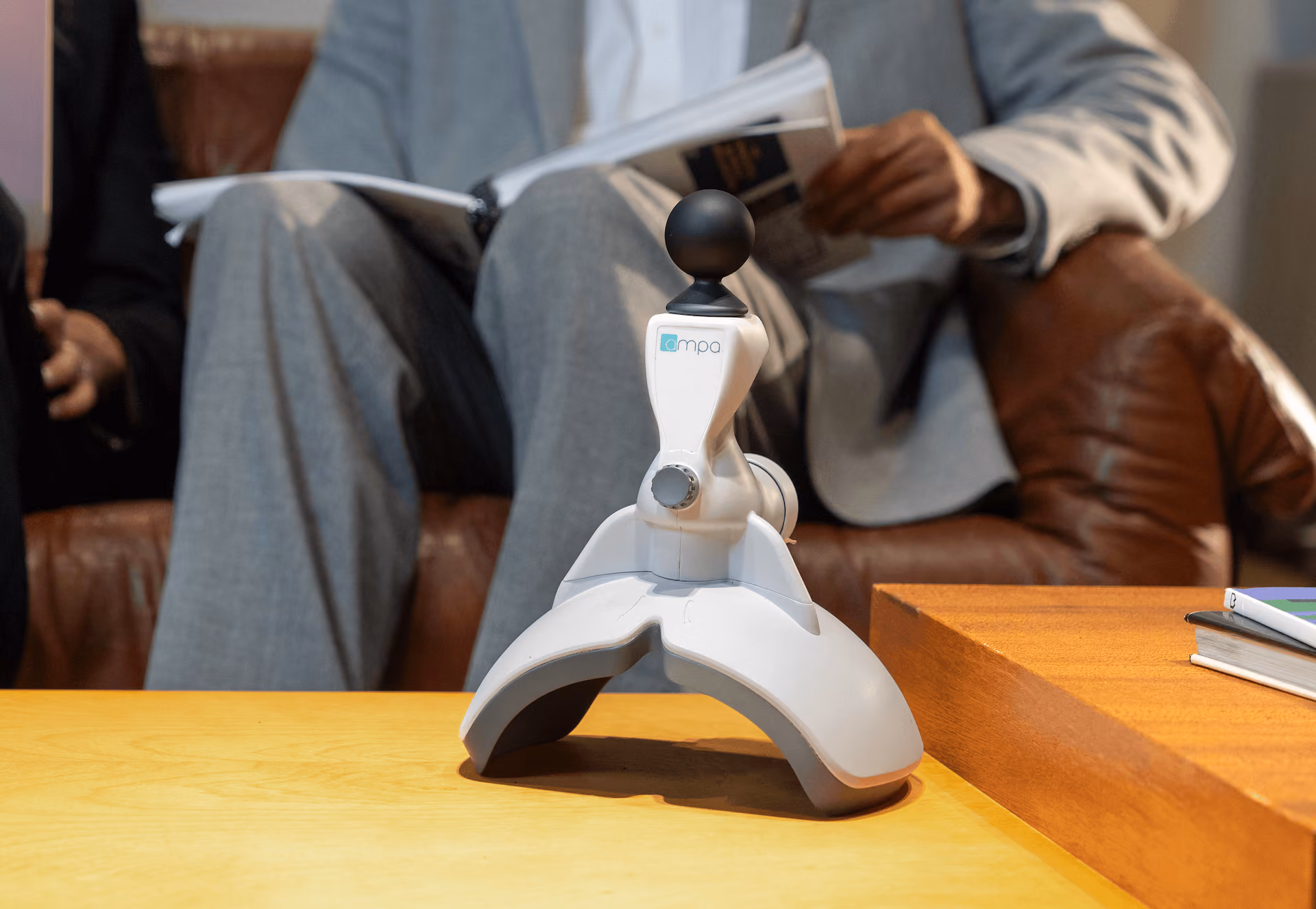 White and gray medical device with a black ball sensor on a wooden table in front of a person reading.