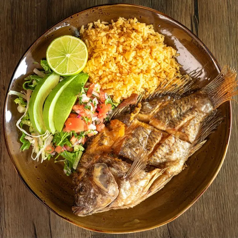 Plate of fried fish with red rice and fresh salad with avocado