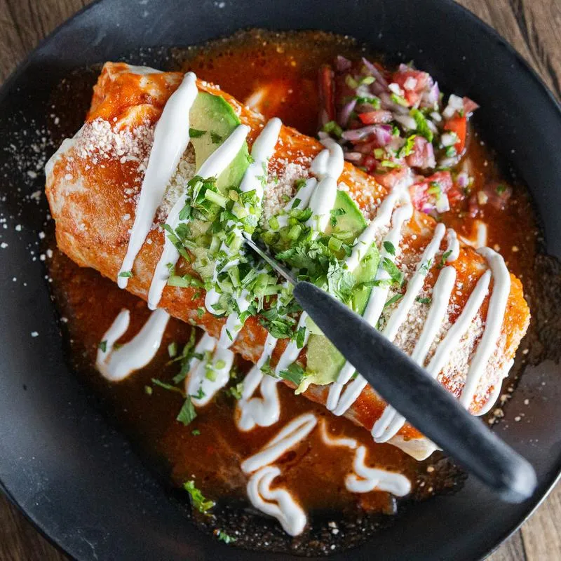 A wet cheese burrito with red sauce cream, avocado and chesee 