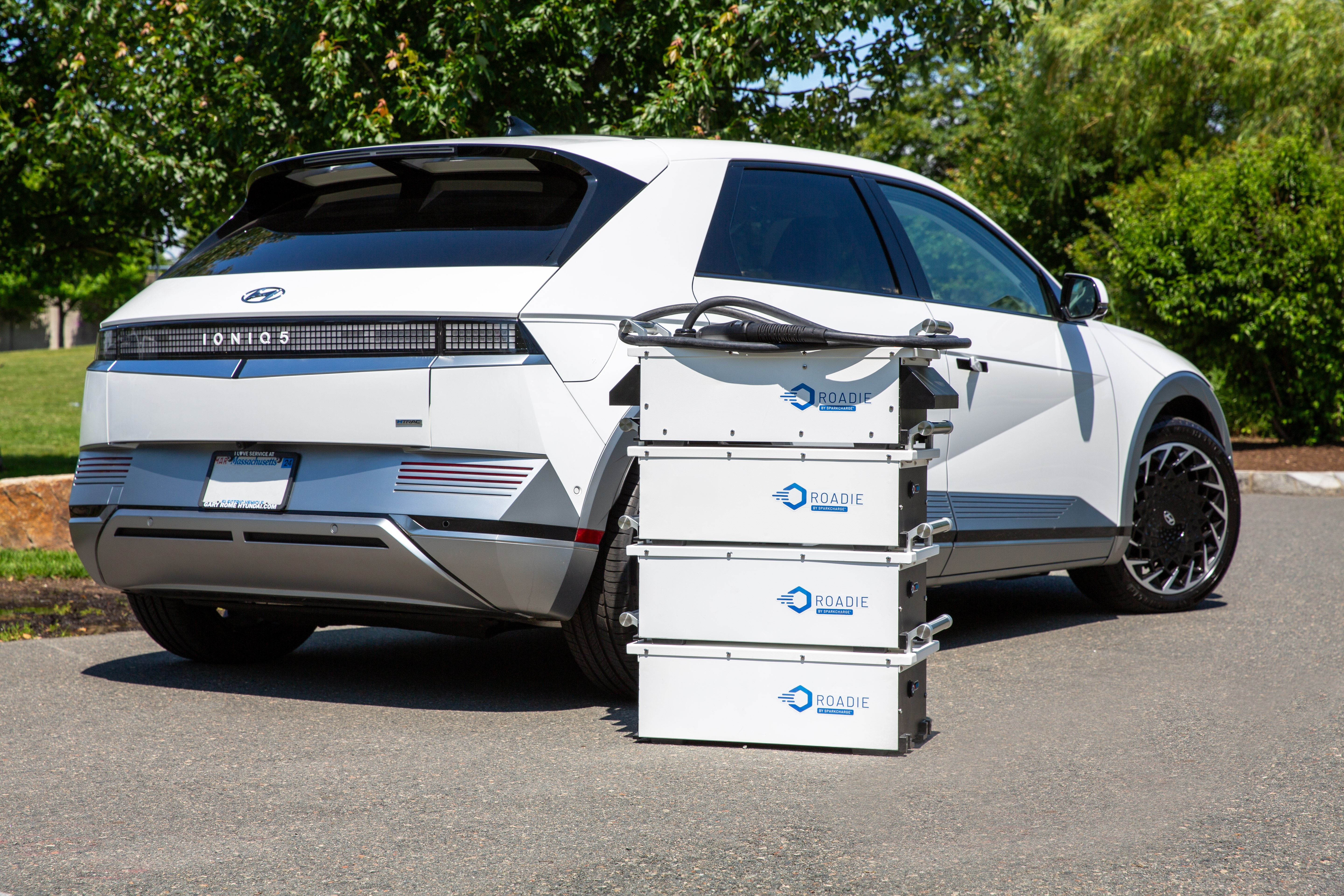 3 Roadie Portable Batteries stacked with 1 Roadie Portable charger in front of an Audi EV charging on the side of the road to prevent the EV from running out of range and reducing range anxiety.