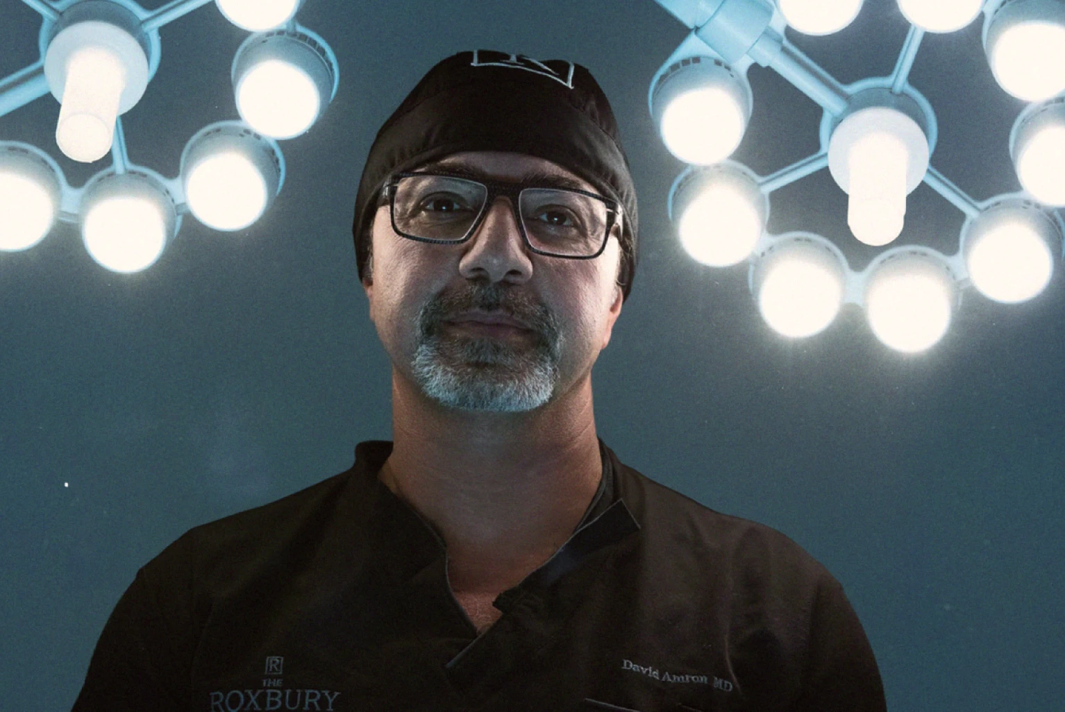 Dr. David Amron wearing surgical scrubs, with large bright lights