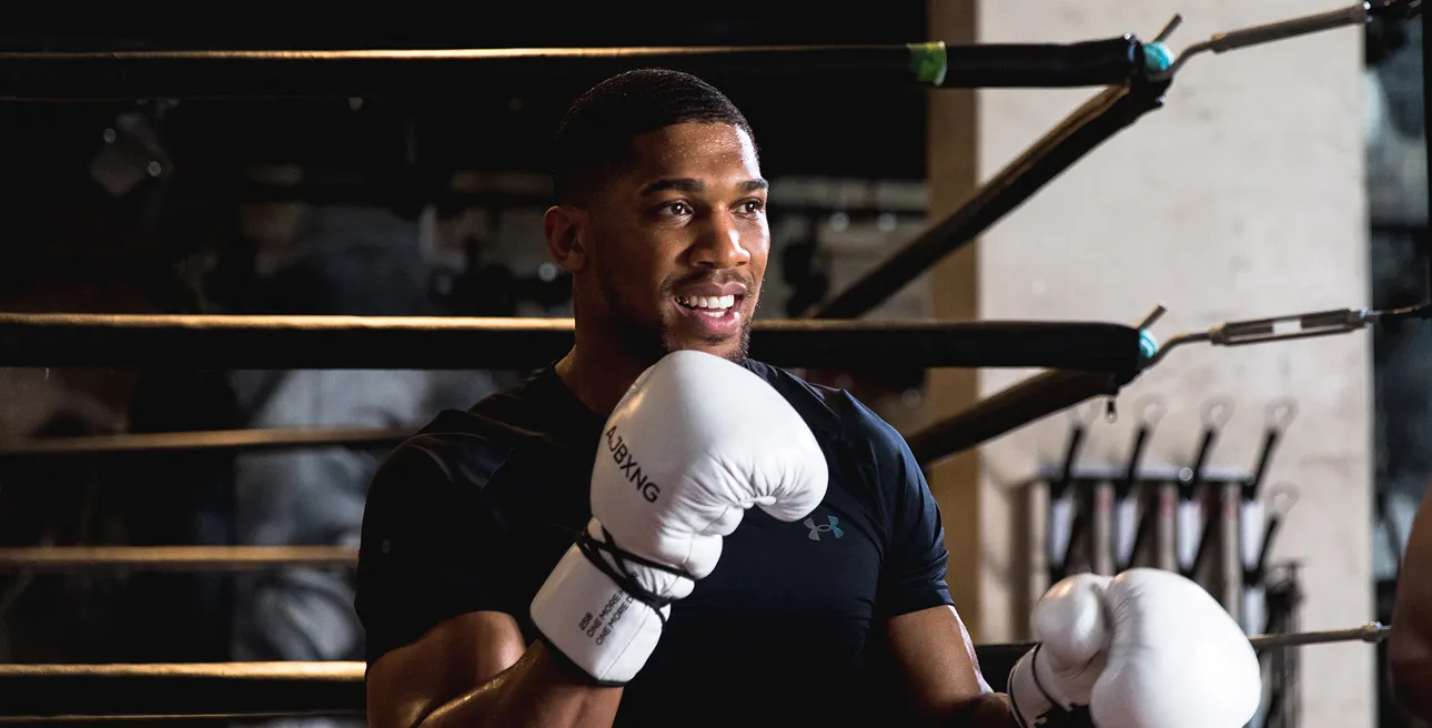 Anthony Joshua in a boxing ring wearing white gloves, capturing the energetic and approachable tone of the campaign