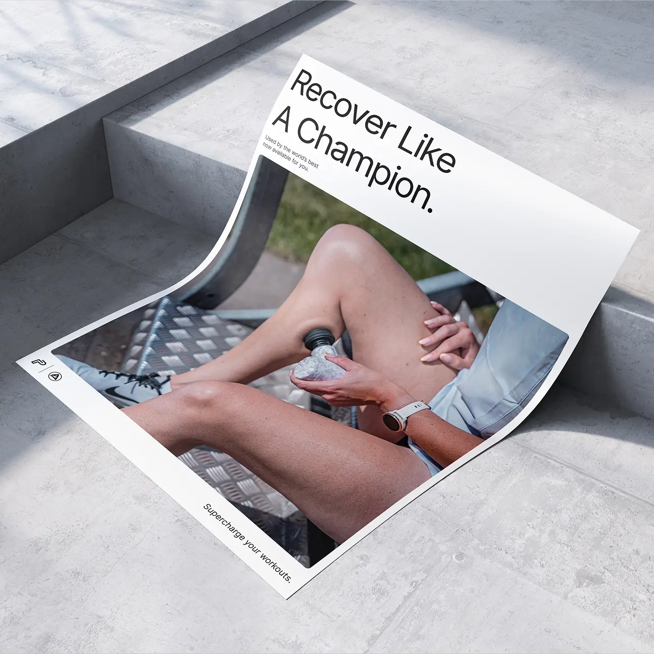 High-angle shot of a printed campaign poster mockup on concrete, featuring lifestyle photography of an athelete using the massage gun.