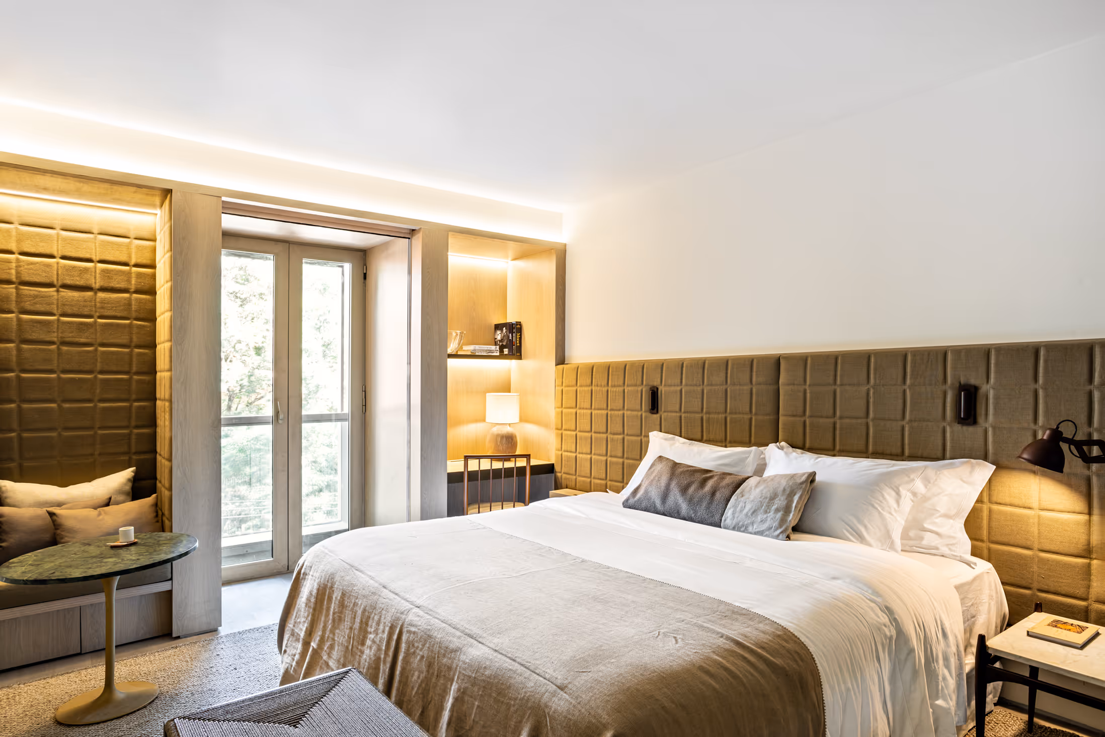Modern luxurious bedroom with a spacious bed and cozy reading nook features brown headboard.