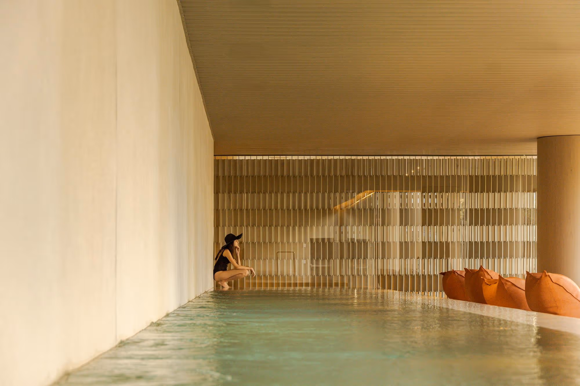 A minimalist indoor pool featuring two stainless steel handrails and calm water, illuminated by soft light against a neutral-toned wall.