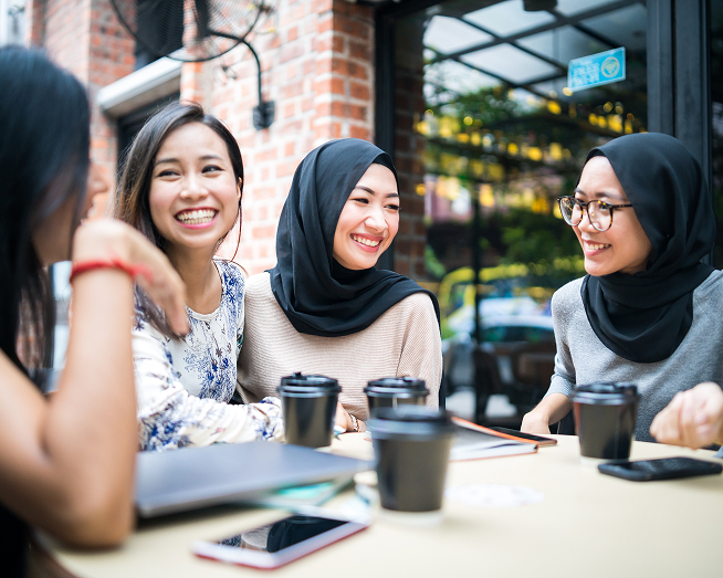 Four friends laughing and talking over coffee at an outdoor café table.