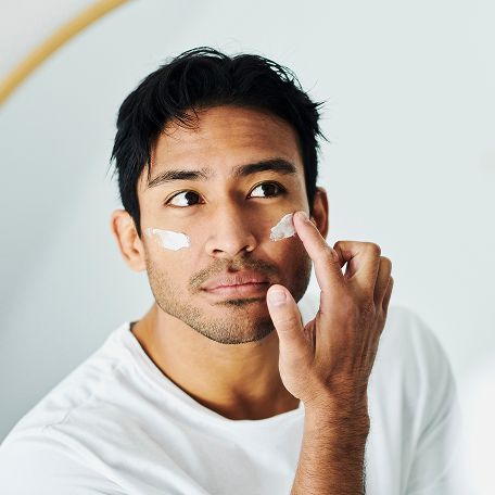 Man applying facial moisturizer while looking in the mirror.