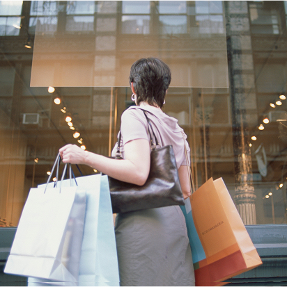 Woman holding multiple shopping bags while looking at a store window display.