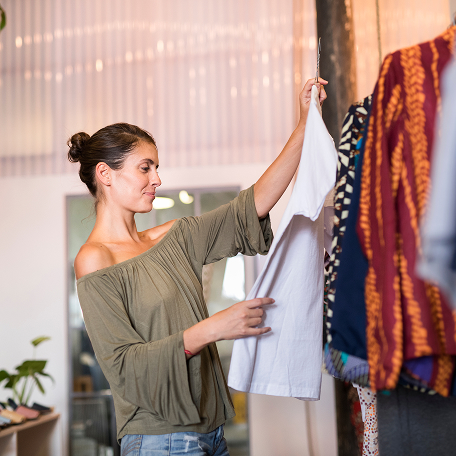 Woman examining a white shirt while shopping in a boutique clothing store.
