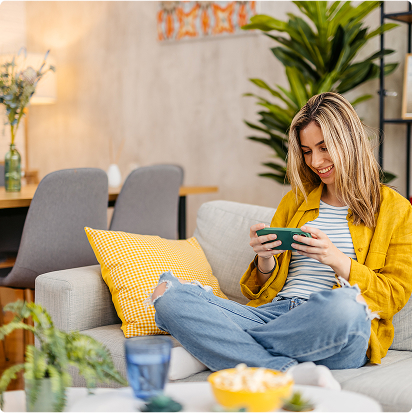 Young woman sitting on a sofa smiling while using her smartphone at home.