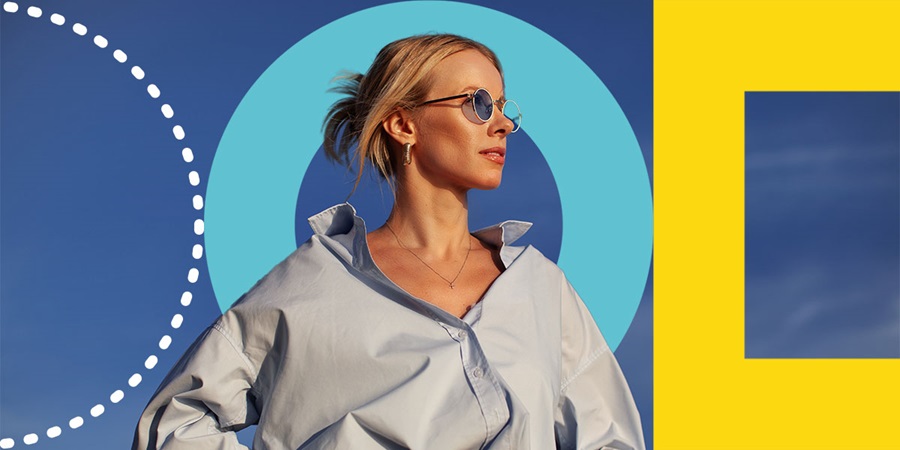 A woman wearing blue-tinted sunglasses and an oversized light blue shirt looks confidently into the distance under a clear sky, with bold geometric shapes in blue and yellow forming a modern background.