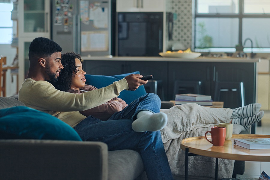 Couple relaxing on a sofa in a modern living room, watching TV and enjoying snacks with coffee mugs on the table.