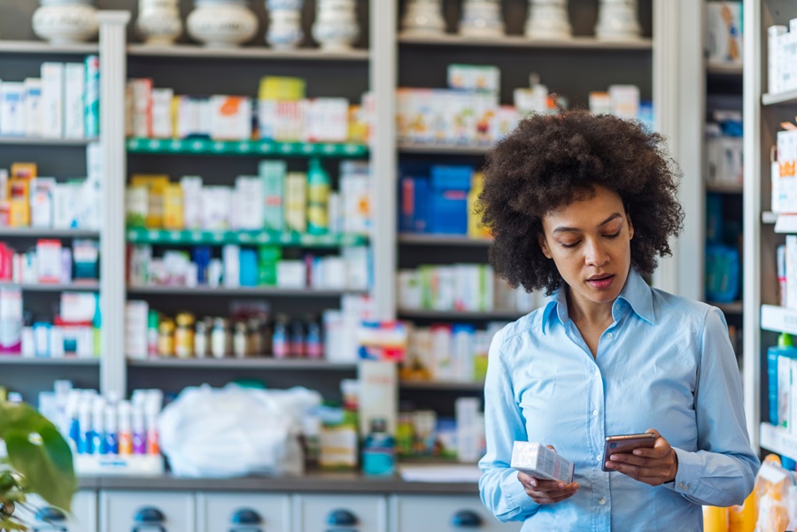 Woman standing in a pharmacy aisle, comparing products and checking information on her smartphone.