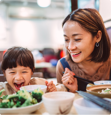 Smiling woman and child enjoying a meal together at a table with bowls of food.