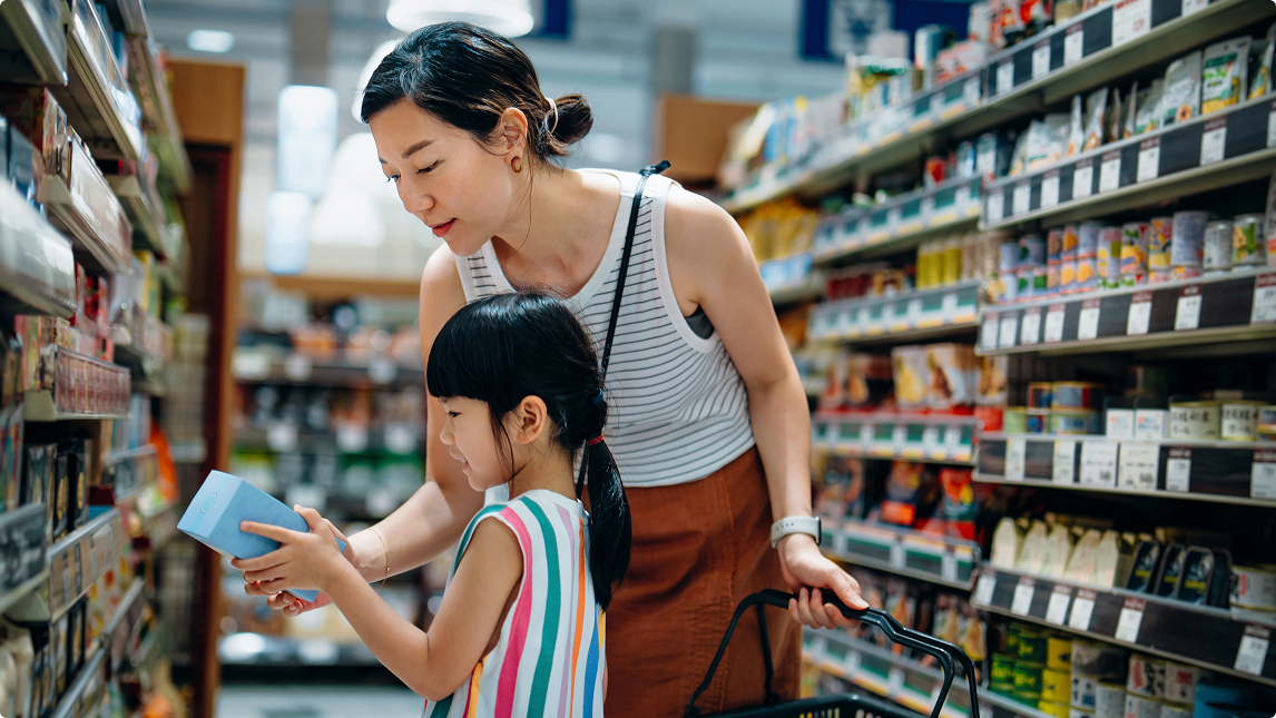 Mother and daughter looking at a product together while shopping in a grocery store aisle.