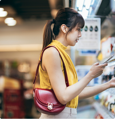 Young woman in a yellow sleeveless top using her smartphone while shopping indoors.