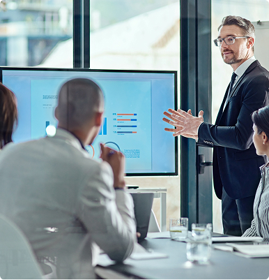 Businessman in suit presenting data with charts on a screen to colleagues in a modern office.