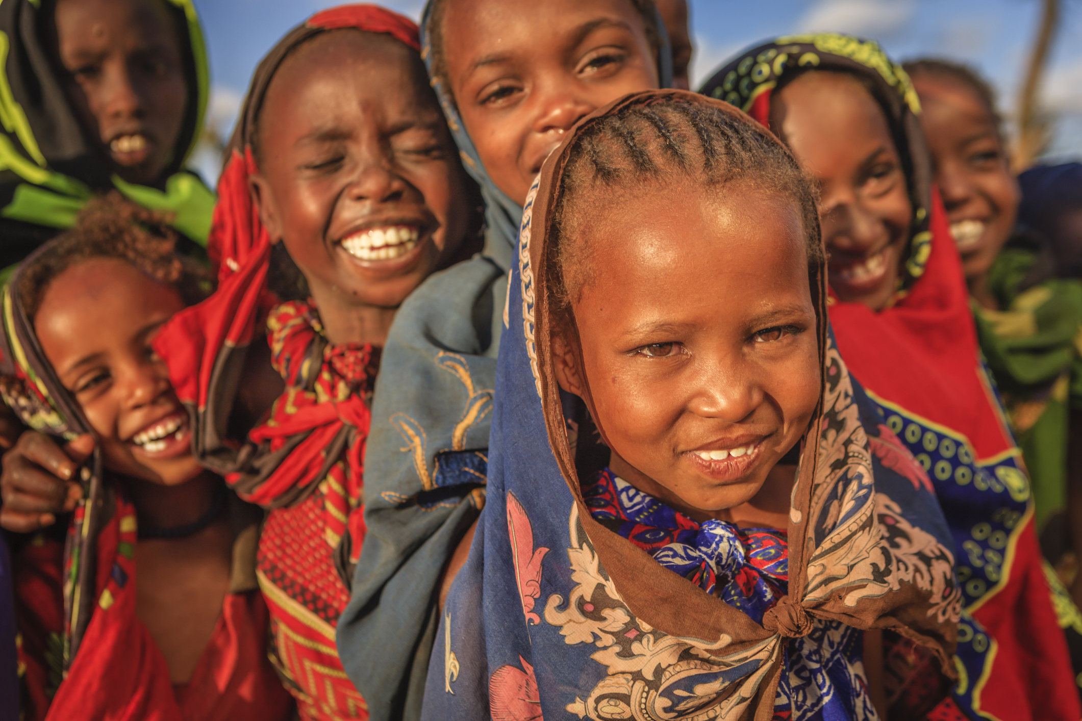 Group of smiling children wearing colorful patterned headscarves and traditional clothes outdoors.