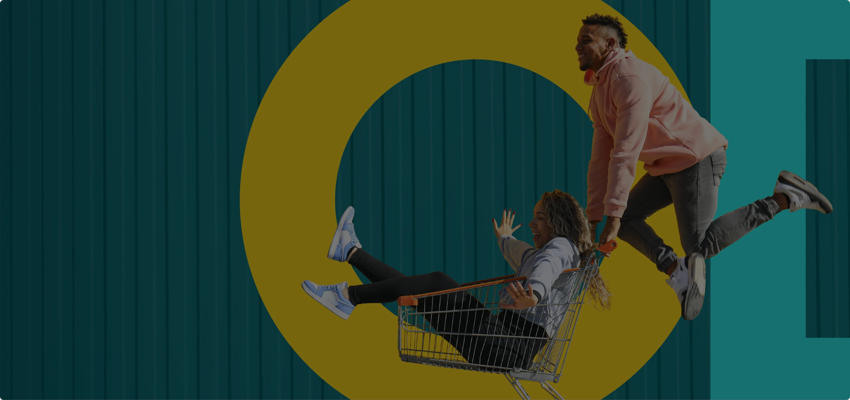 Man pushing smiling woman sitting in shopping cart in front of large yellow circle on teal background.
