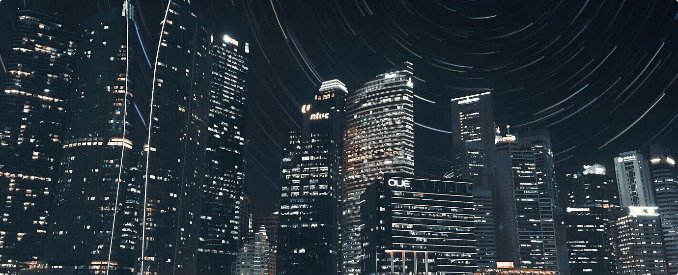 Night cityscape with illuminated skyscrapers under a sky showing star trails in circular patterns.
