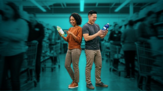 A woman and a man stand back to back, each holding and examining a product bottle with smiles in a store aisle, with blurred shoppers and shelves in the background.