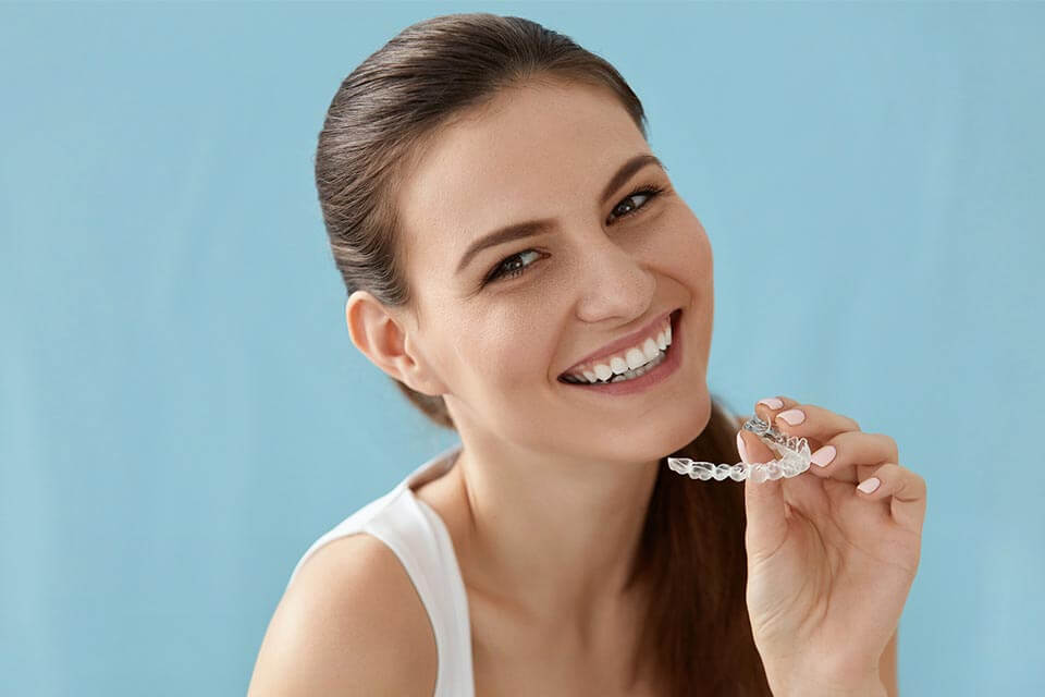 Invisalign in New York, NY | woman smiling holding an Invisalign Tray