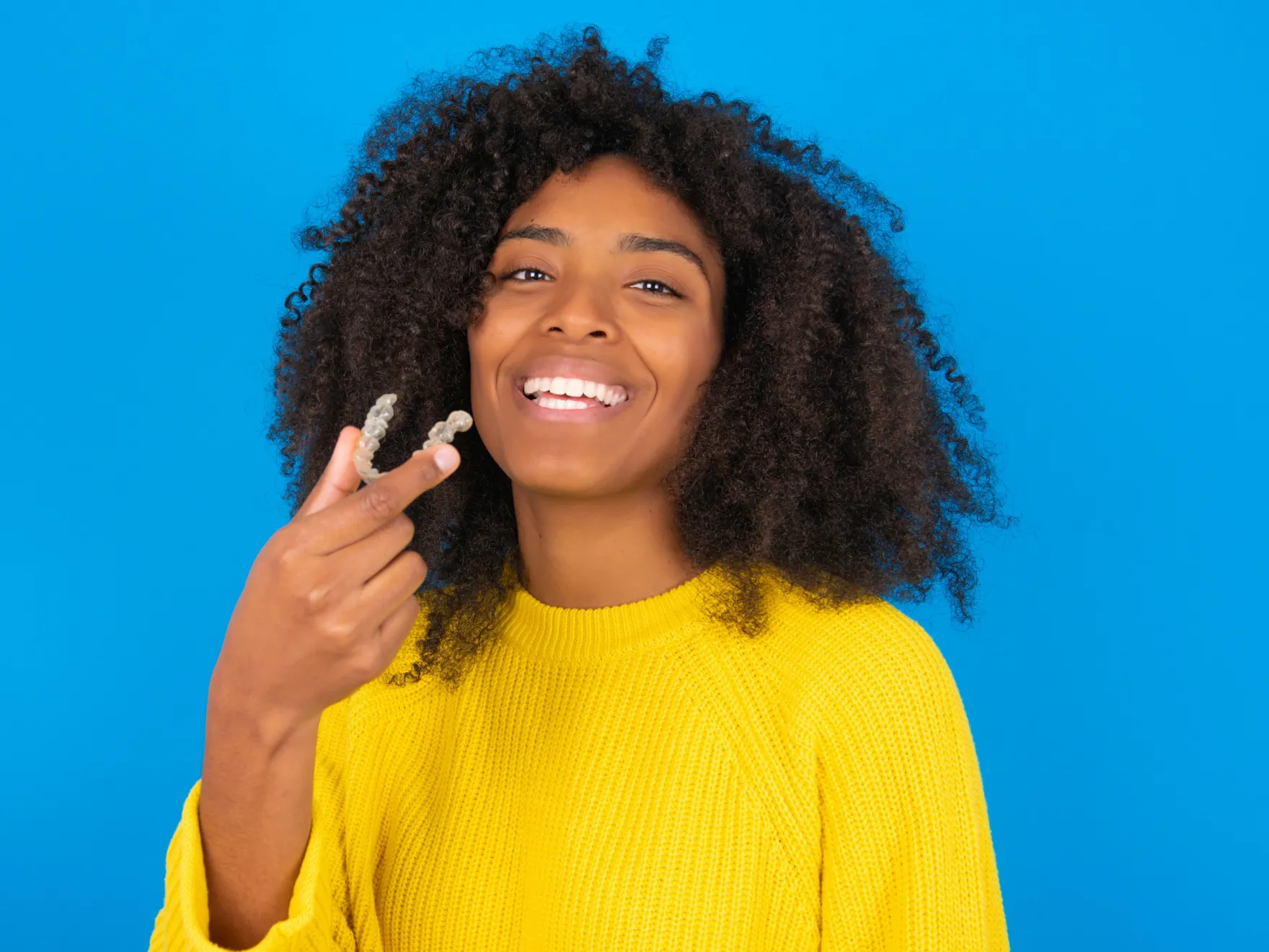 Invisalign in New York, NY | woman smiling holding an Invisalign Tray