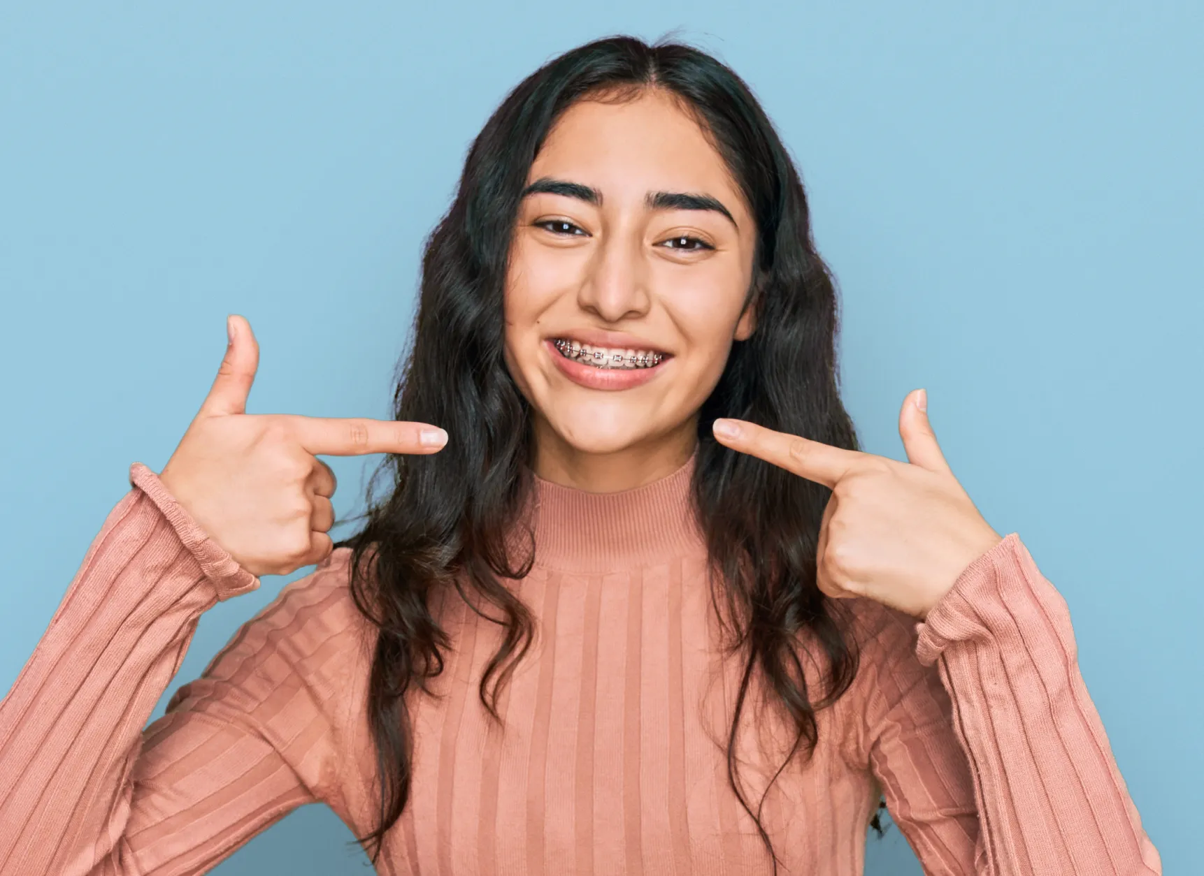 young woman with braces pointing at her smile