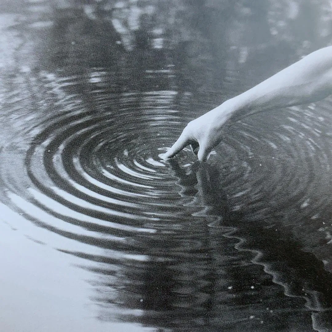 Black and white image of a finger in water causing a ripple