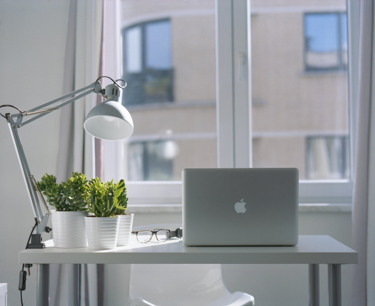Minimalist workspace with MacBook, desk lamp, succulents, and glasses