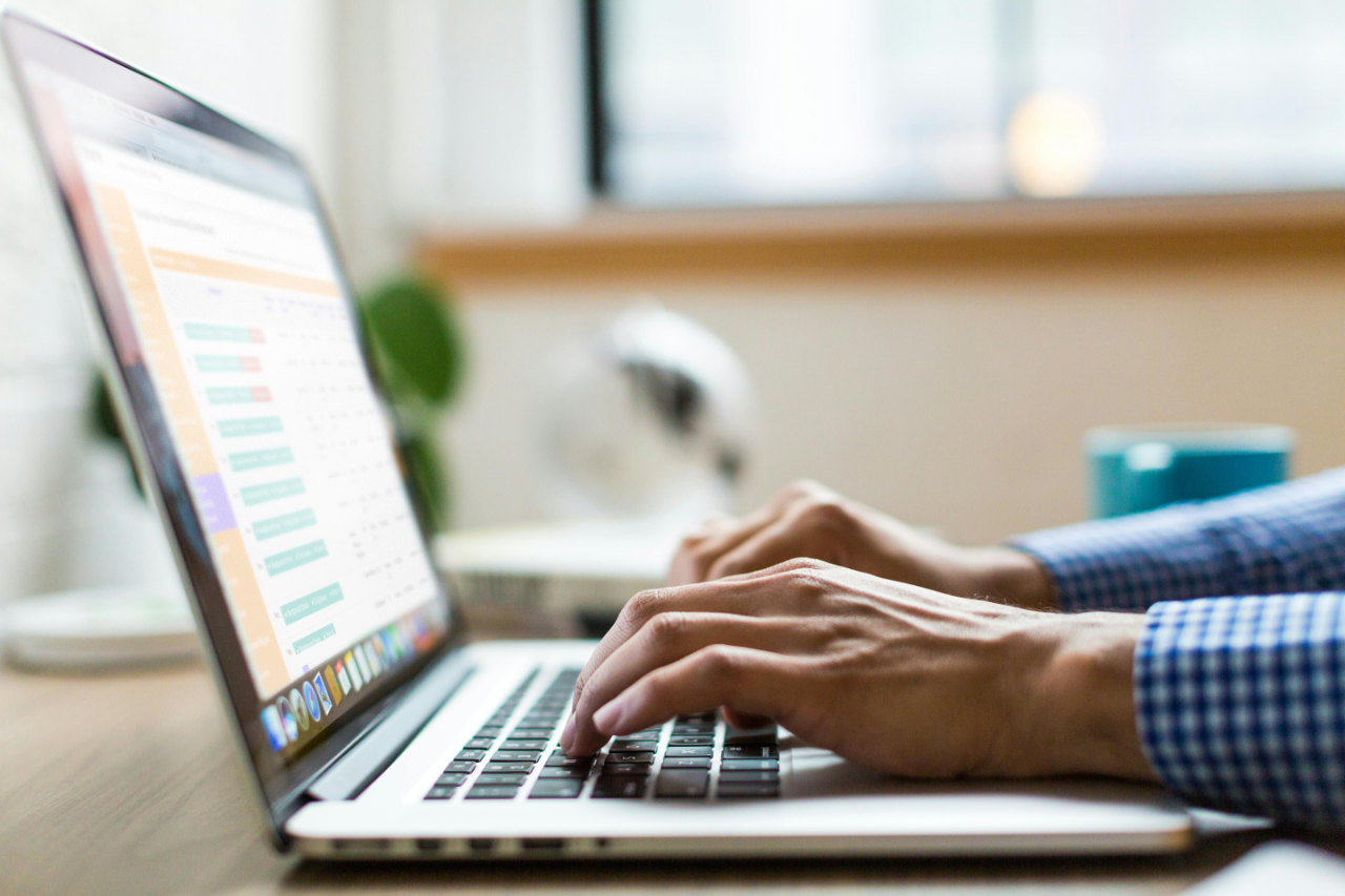 Hands typing on laptop keyboard with spreadsheet on screen