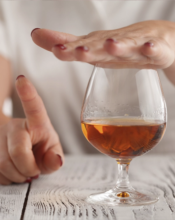 O mână gesticulează stop deasupra unui pahar cu băutură alcoolică, în timp ce un deget arată, simbolizând refuzul sau renunțarea la alcool.