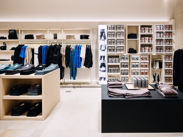 Modern clothing store interior with neatly folded jeans on shelves and racks of shirts and jackets.