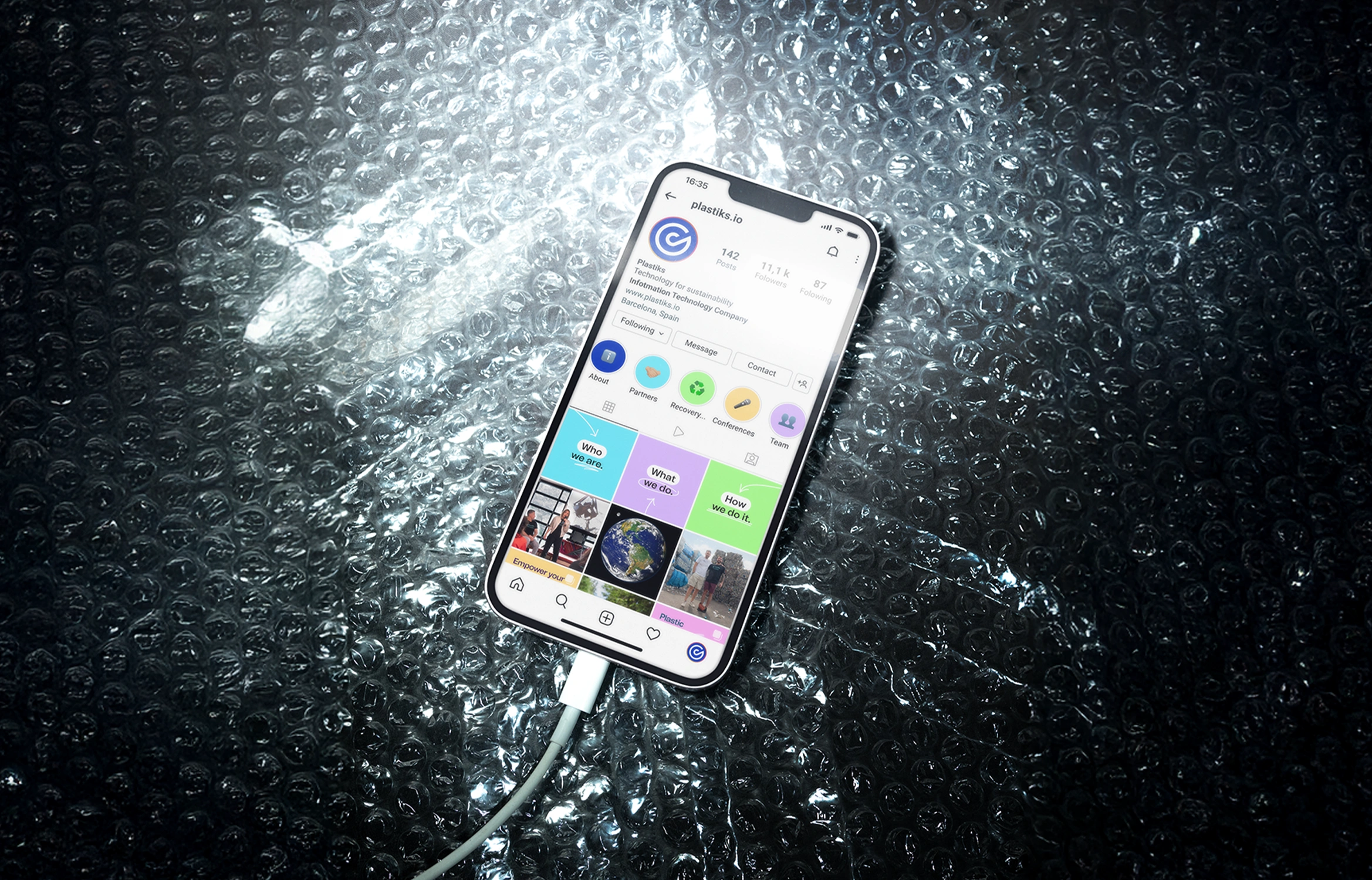 Smartphone displaying an Instagram profile with sustainability content, placed on reflective bubble wrap and connected by a charging cable.