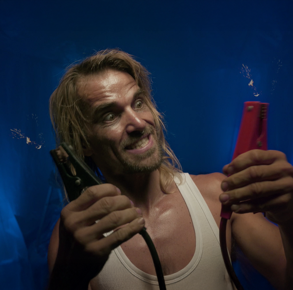 Man with intense expression holding sparking jumper cables against a dark blue background.