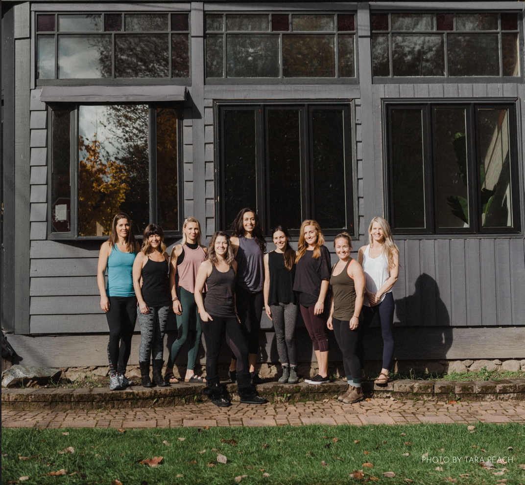 group of nine women standing in-front of a grey building with large windows