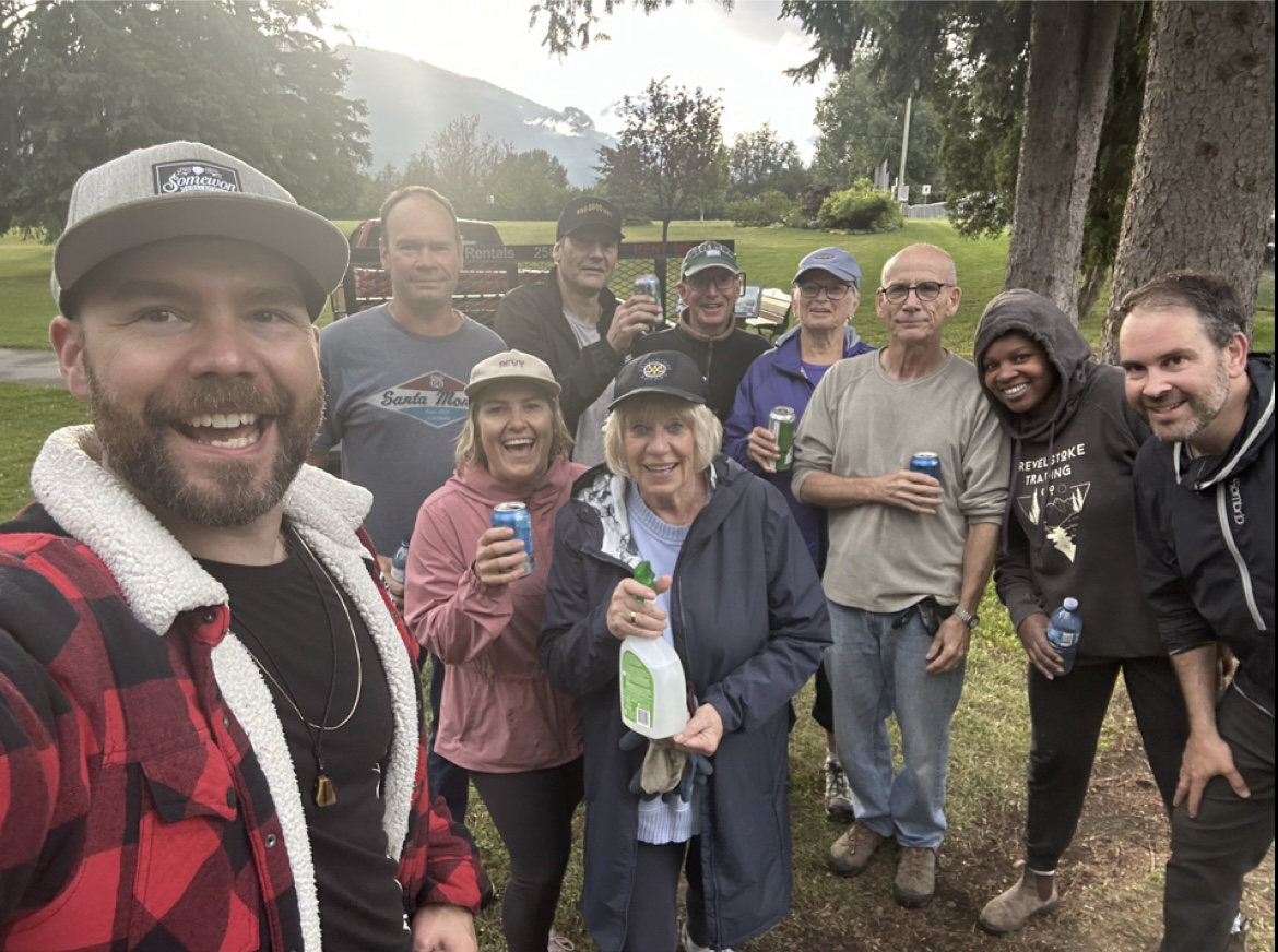 a group of people smiling and posing for a selfie while holding beers at a social gathering
