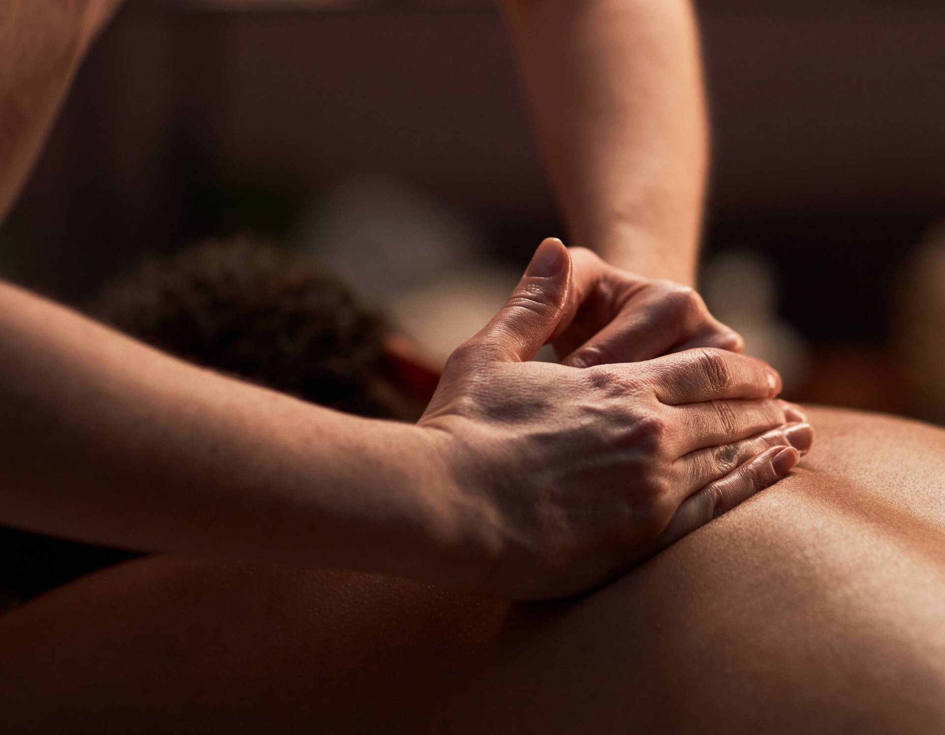Therapist's hands giving a back massage to a person lying face down with blurred background.