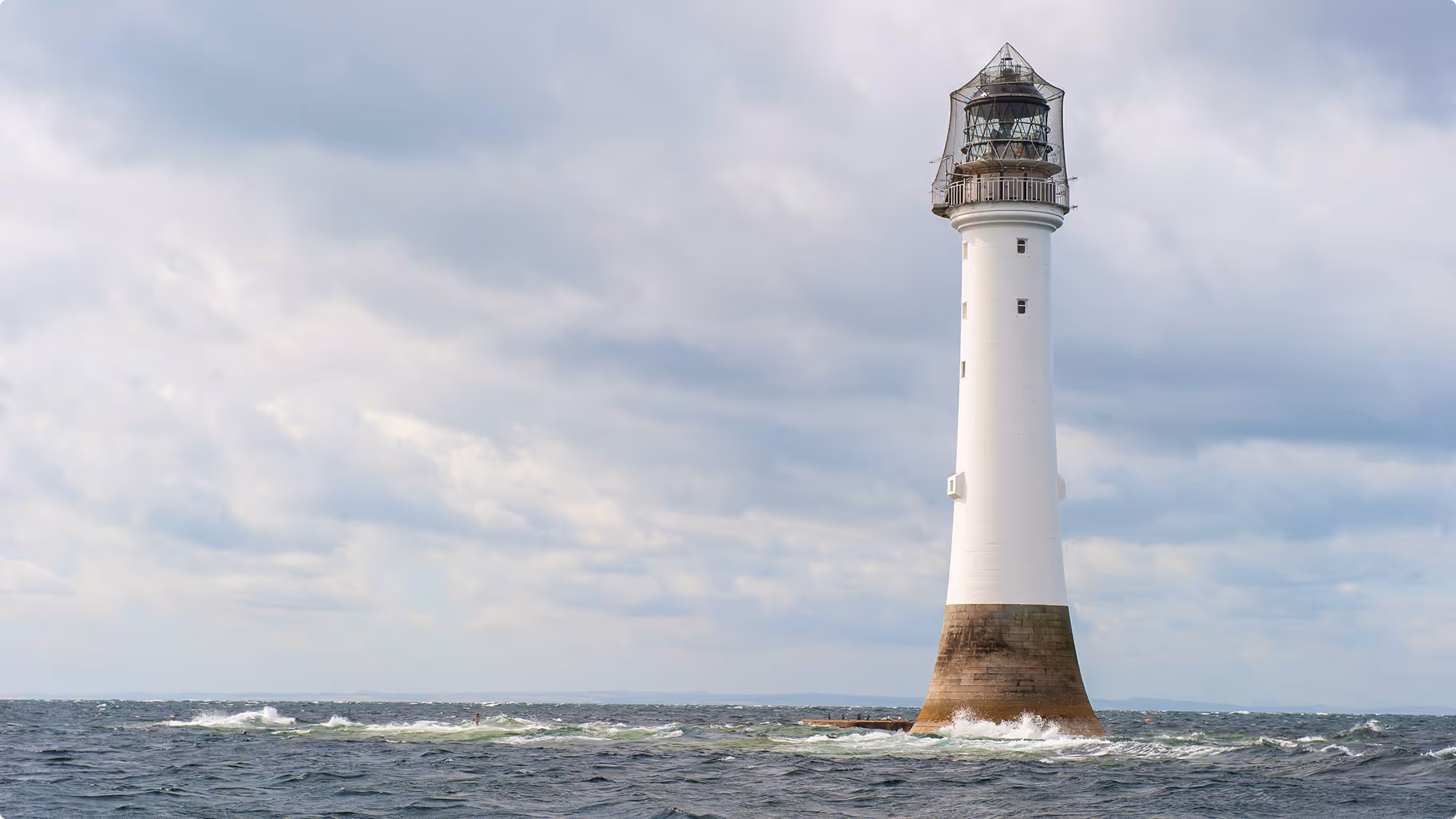 Bellrock lighthouse, silhouetted against a darkening sky as the sun sets.