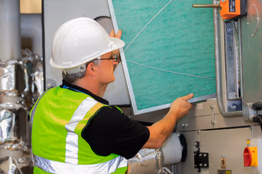 A man in a hard hat and hi-vis jacket is removing a panel for inspection